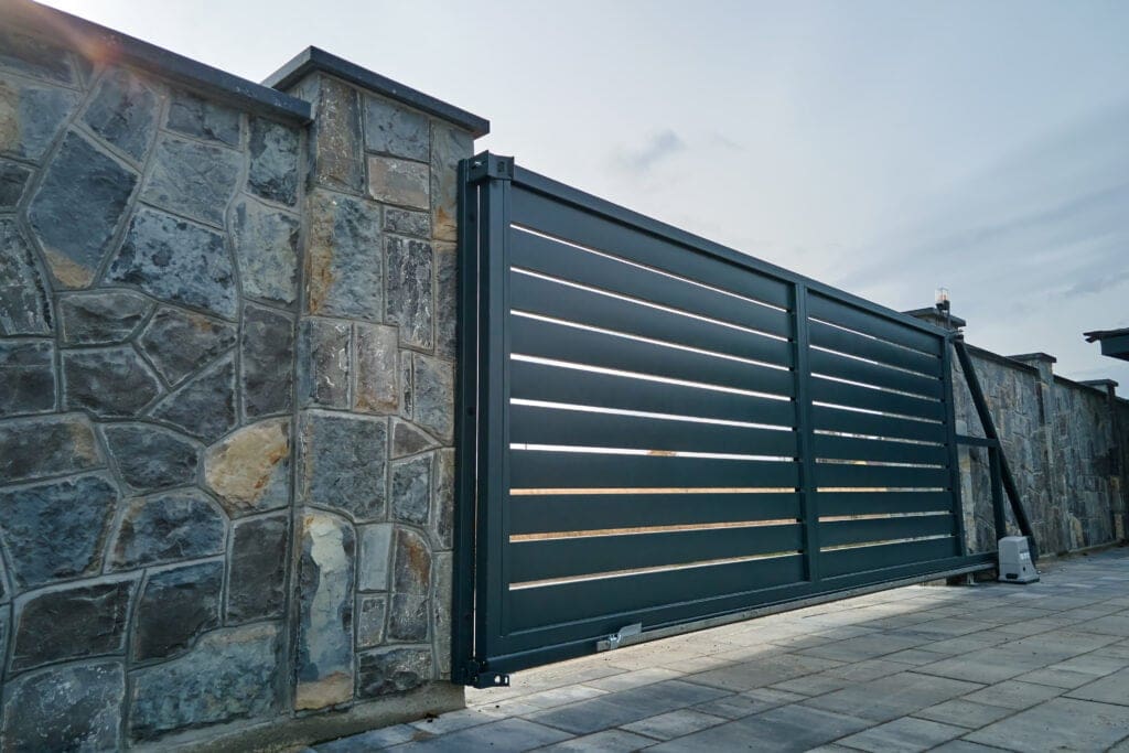 Wide automatic sliding gate with remote control installed in high stone fense wall. Security and protection concept.